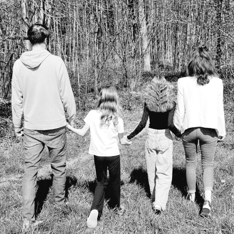 Eine Familie läuft Hand in Hand auf einen Wald zu in einem Schwarzweiß-Foto